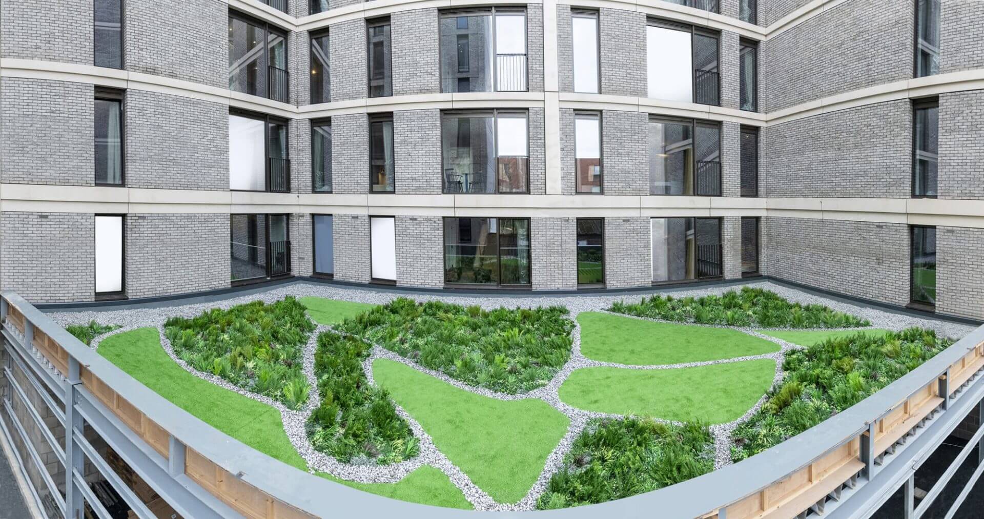 A modern building courtyard in Manchester showcases large windows and an innovative artificial roof garden. Neatly arranged patches of grass and plants, outlined with small stones, create an abstract pattern, embodying the essence of a cutting-edge UK Roof Garden Project.