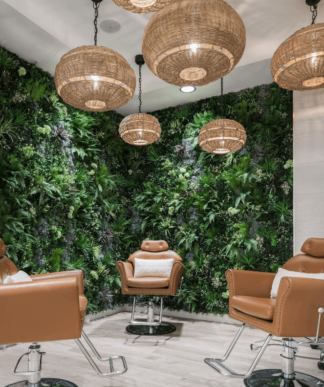 A modern salon interior showcases brown leather chairs, a lush living green wall, and elegant wicker light fixtures. The wooden floor and neutral tones amplify the warm, inviting atmosphere with an artificial touch.