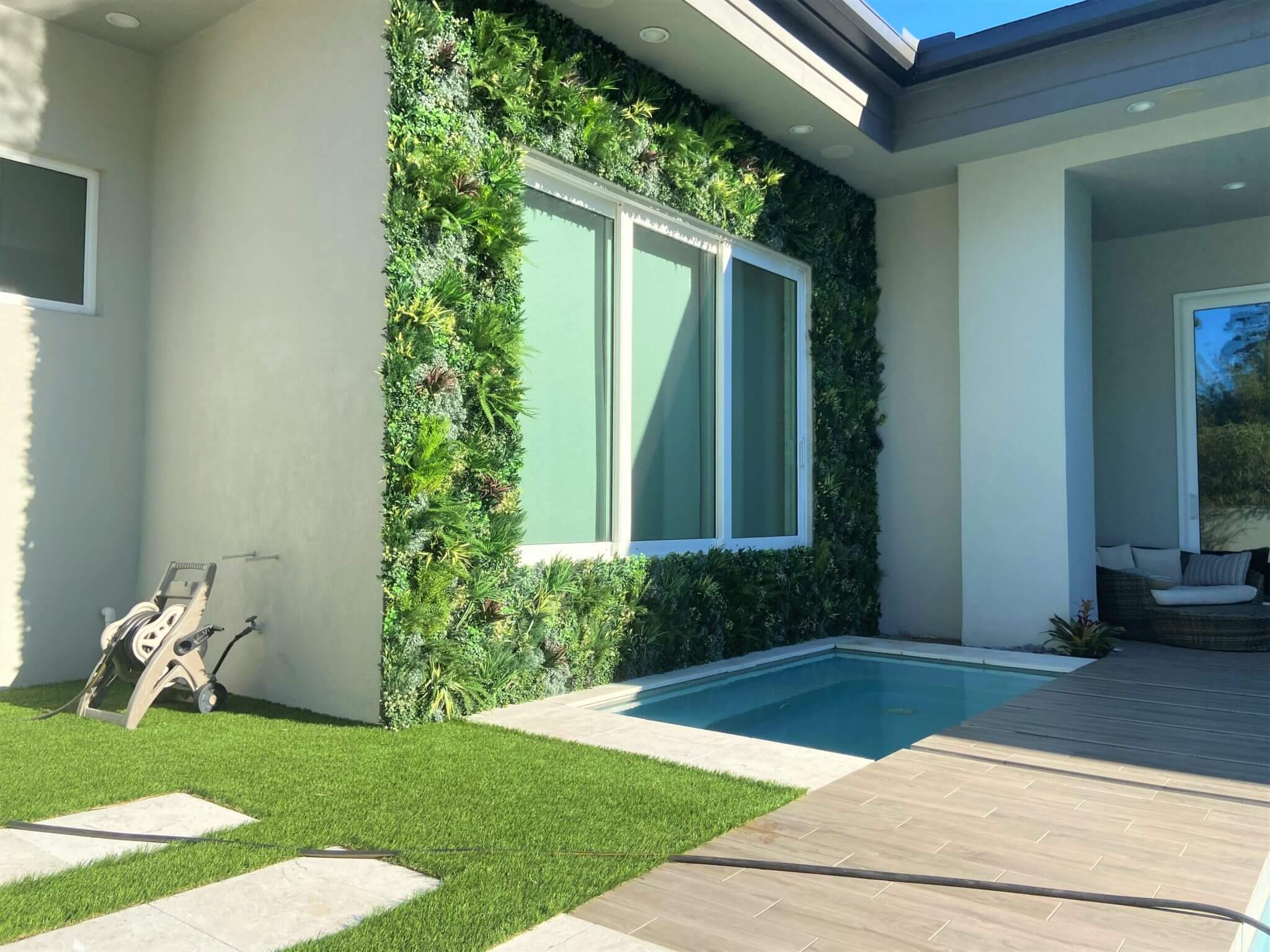 A modern house exterior in Denver, Colorado, showcasing a small rectangular pool beside a lush vertical garden wall. The space is accented with greenery on the wall and neat pathways leading to the entrance, perfectly complementing its serene rooftop garden ambiance.