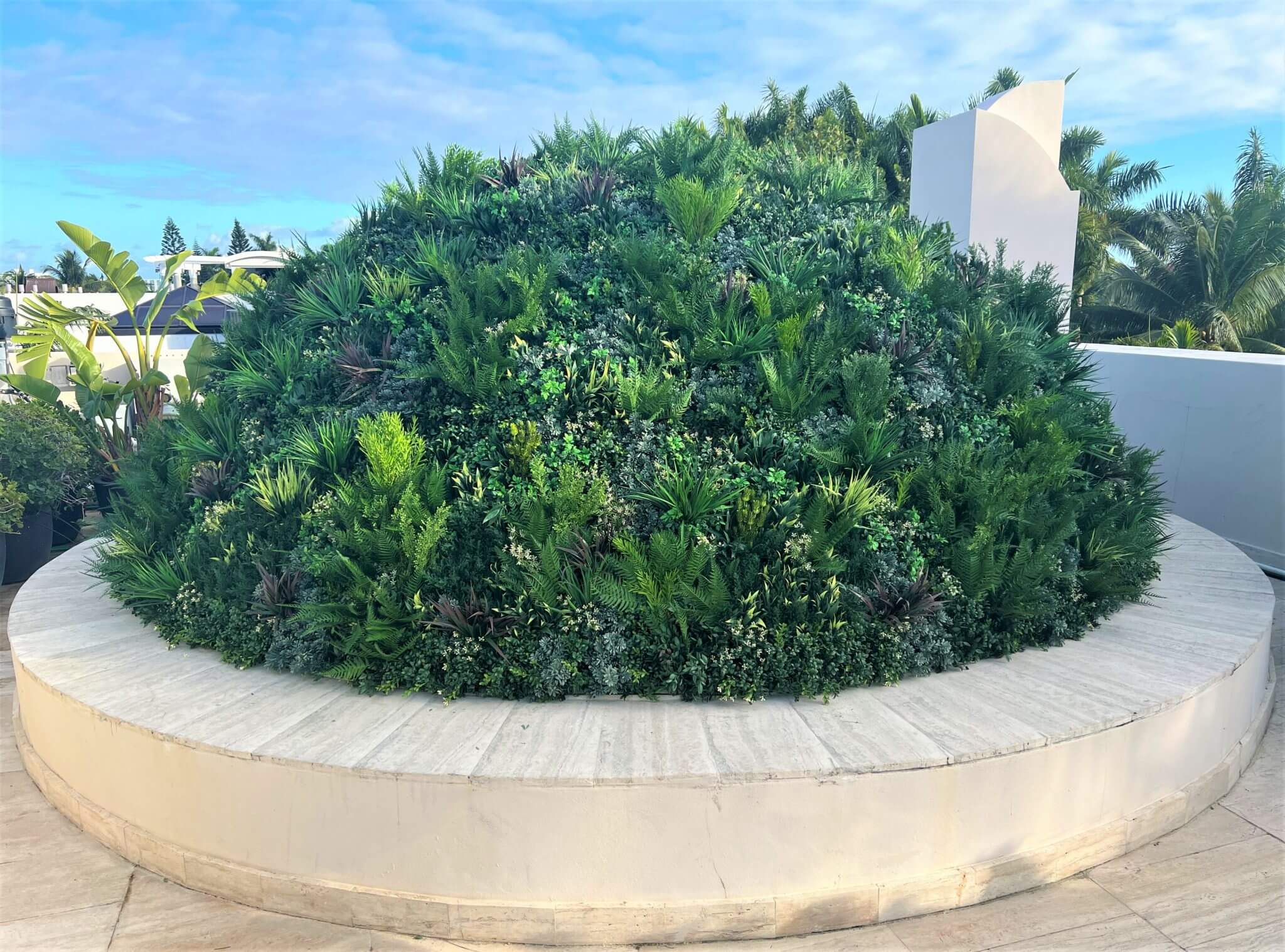 A terraced garden with lush greenery and various plants flourishes in a circular stone planter, set against the clear Florida sky. This scene evokes the innovative spirit of dome green wall installations in Miami, where nature seamlessly blends with urban design.