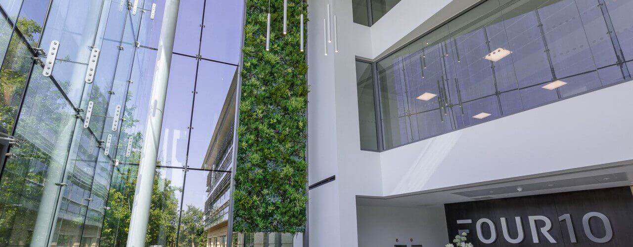 The modern building interior features large glass walls, a vertical garden, and high ceilings. The number FOUR10 is prominently displayed on a wall. With bright lighting and an artificial touch, the clean design creates an open, airy atmosphere.