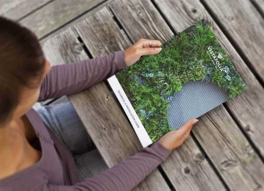 A person in a purple shirt is holding a brochure with a cover featuring a lush green plant design and the words USA Florals on it. The person is sitting at a wooden table.