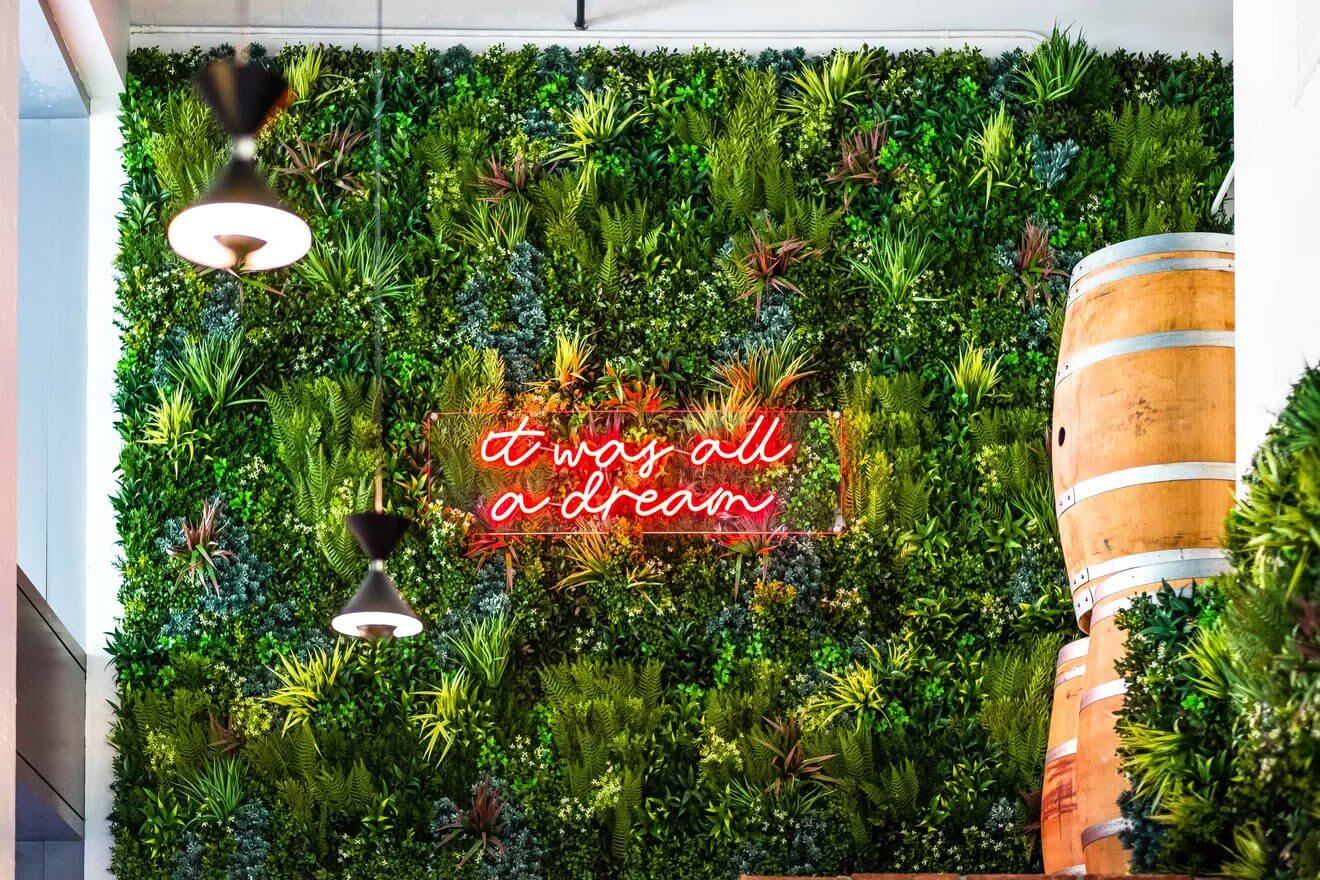 A lush green plant wall with a neon pink sign reading 