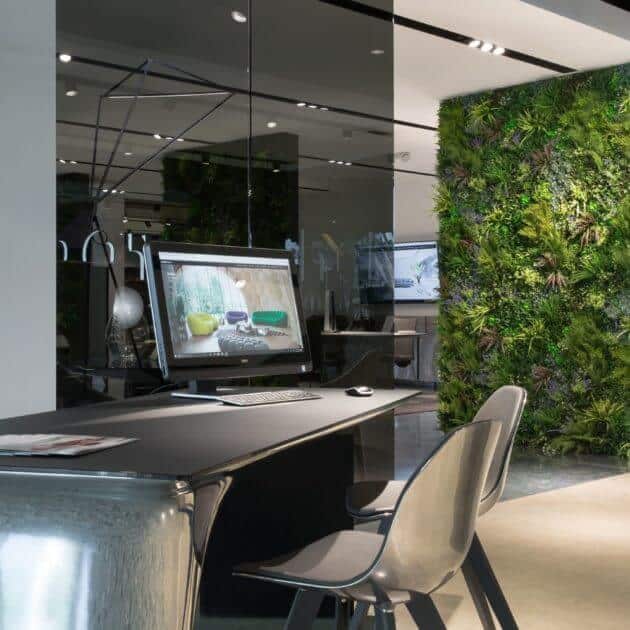 A modern office space with a sleek desk and chair. A computer monitors vibrant nature images. A vertical green wall with various plants decorates the background, adding a touch of nature to the contemporary setting.