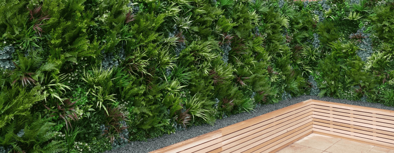 An artificial lush green vertical garden on a wall, filled with various types of plants, sits next to wooden bench seating in a corner. The scene is tranquil and vibrant with greenery.