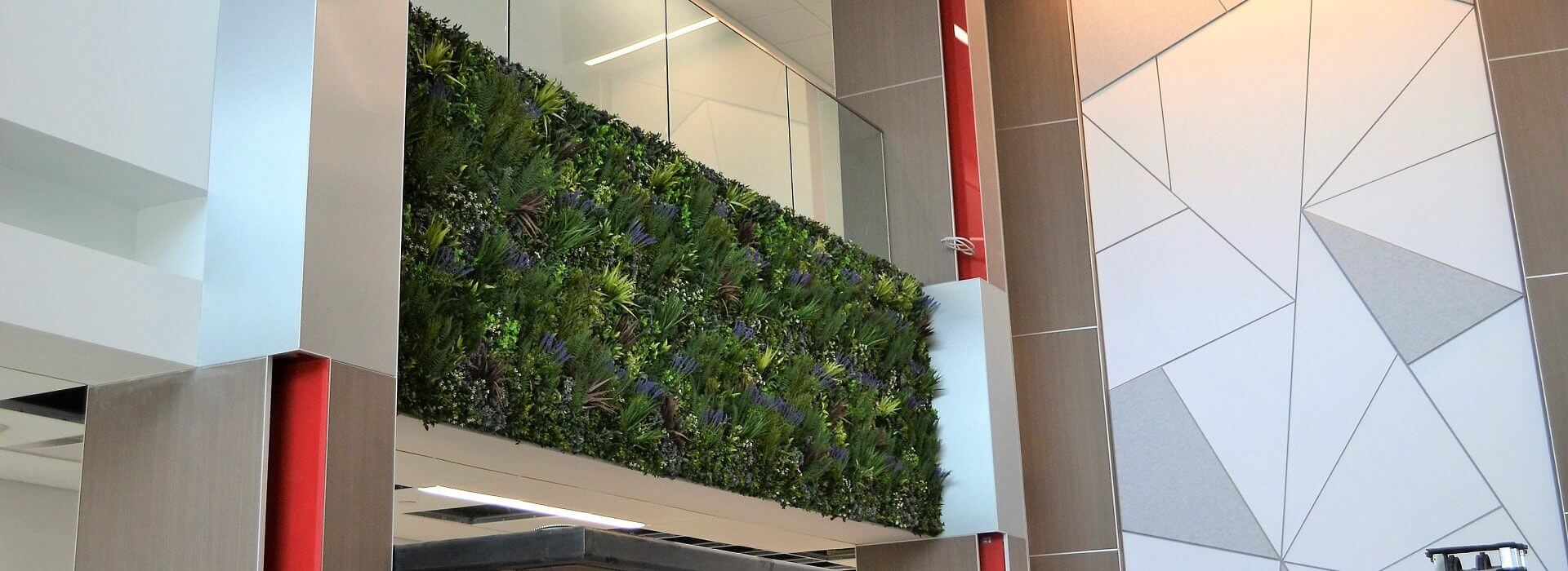 A modern interior in Des Moines, Iowa, showcases an internal green wall with lush foliage. The space features geometric patterns on adjacent walls, red pillars, and a ceiling with recessed lighting, creating a harmonious blend of nature and design.