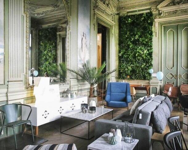 A luxurious room with ornate decorative walls and a large vertical garden. The room is furnished with modern sofas, armchairs, and marble-topped coffee tables. A few blue balloons add a whimsical touch to the elegant space.