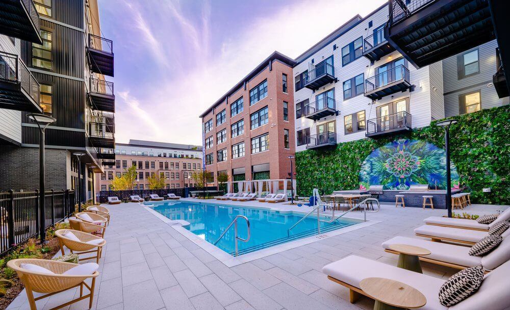 A modern luxury apartment block in Beckert’s Park, Washington DC, boasts a swimming pool framed by lounge chairs. A colorful mural graces a green wall, while multi-story buildings with balconies stand proudly under the vibrant sky.