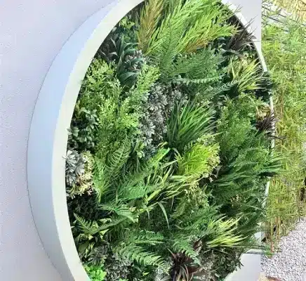 A circular vertical garden, reminiscent of a West London green wall, hangs on the wall, filled with various green plants and ferns to create a lush, natural display.