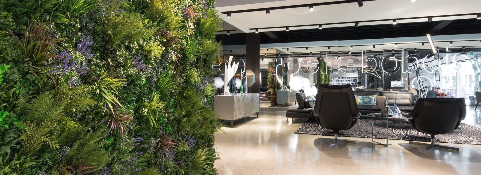 Modern interior in the Roche Bobois showroom, Hollywood, California, featuring a stunning green wall and stylish furniture like black chairs and a sofa. Large windows flood the space with natural light, while a neon sign adds a contemporary touch.