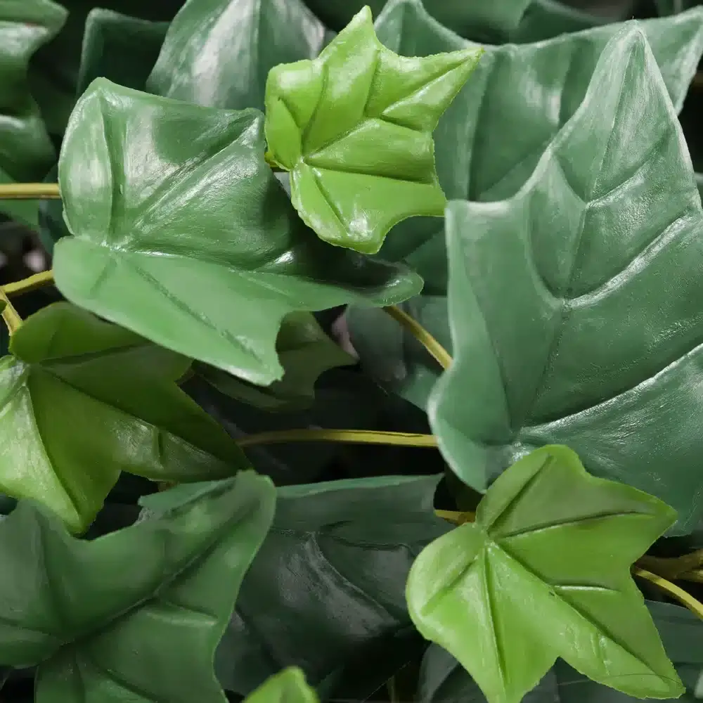 Close-up of several vibrant green artificial leaves, part of the Trailing Ivy Texture Box, showcasing distinct veins and varied shapes densely arranged. The glossy surfaces of these synthetic leaves suggest a plastic material, layered over one another to create a lush appearance.