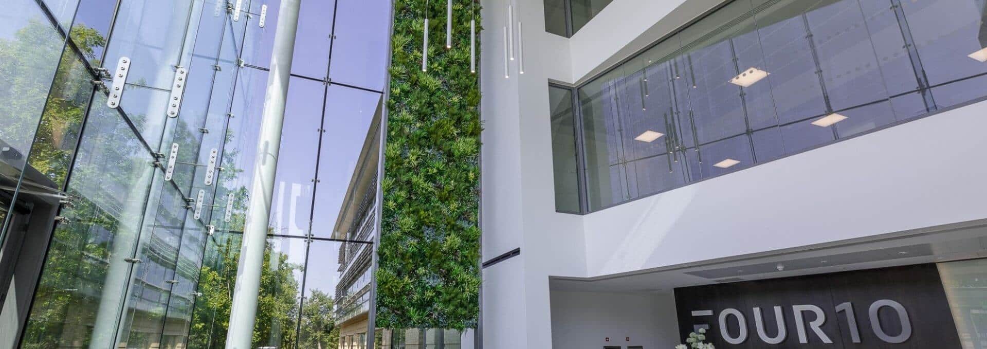 Modern building interior with a glass facade, tall green plant wall, and FOUR10 signage visible. Natural light floods the spacious area, highlighting sleek architectural lines and reflective surfaces. This stunning space in Reading, UK features a vertical garden that enhances its contemporary charm.